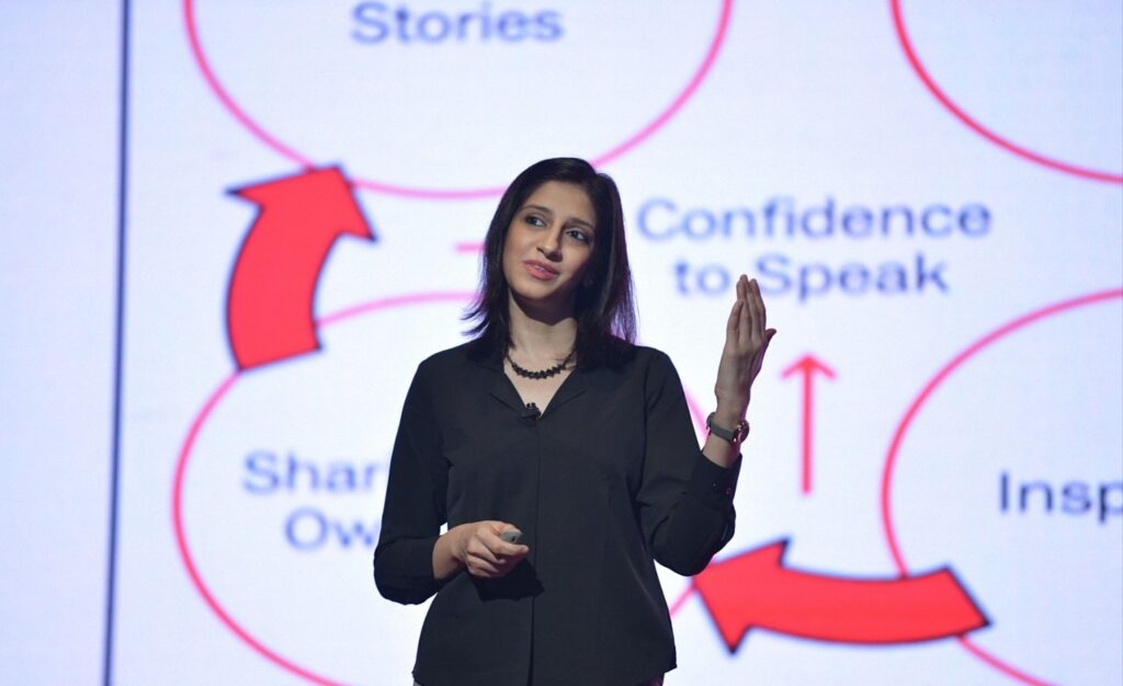 Speaker delivering a TEDx talk on stage, standing confidently under spotlight.